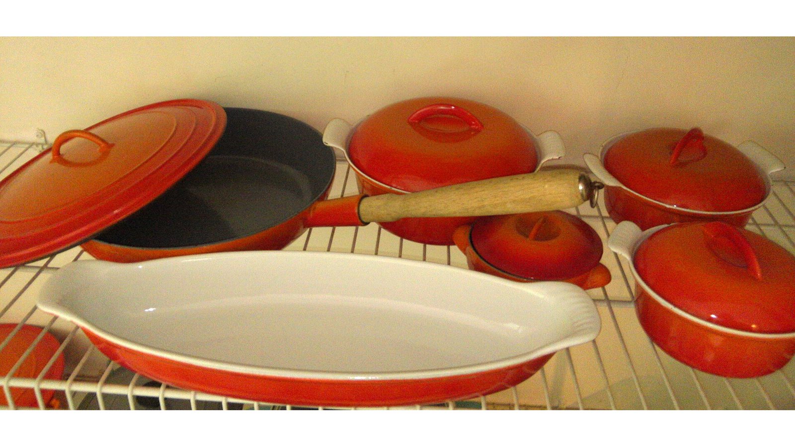 Vintage enameled cast iron pots and pans in several colors on a shelf