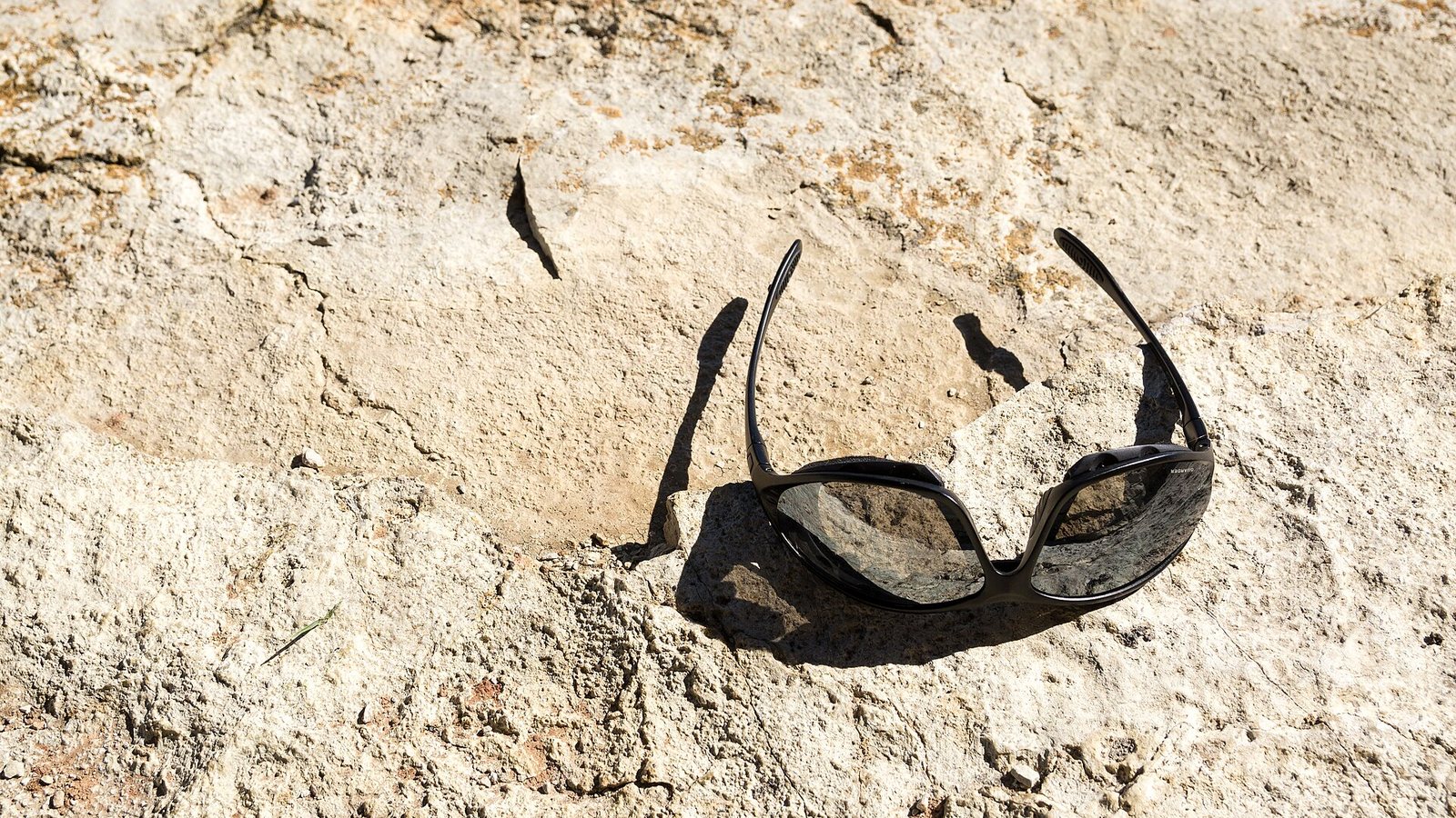 A pair of black sports sunglasses resting on a sunlit rock